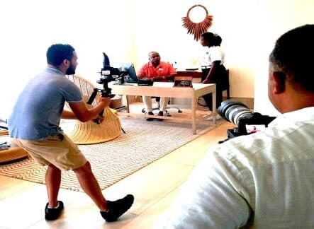 A camera operator filming a young woman working at a hotel concierge desk.