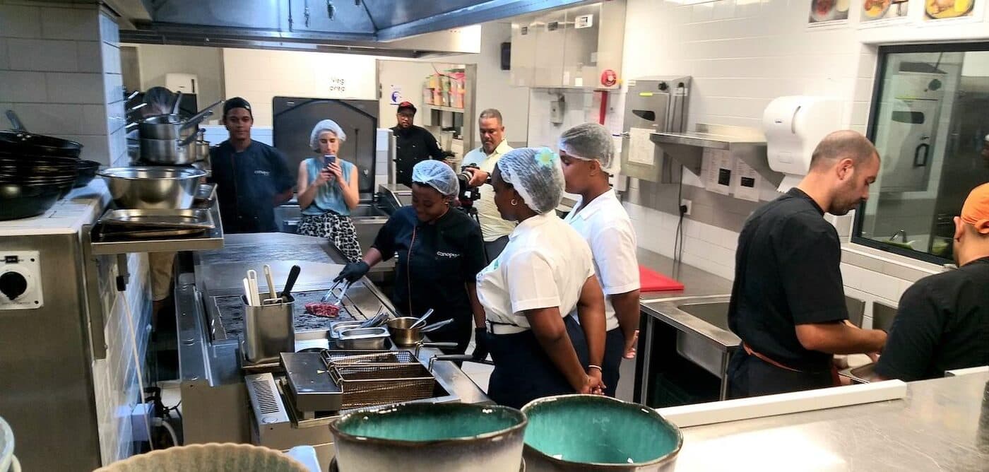 A busy hotel kitchen brigade at work, with a film crew observing from the pass.