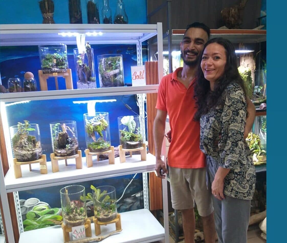 Armaan and Larissa Shah standing beside illuminated shelving displaying a range of planted glass terrariums in the AquaTerra studio.