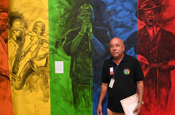A visitor standing in front of a large multi-panel painting of musicians in vivid yellow, green, blue and red.