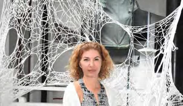 A woman standing inside a gallery installation of white knotted netting stretched across the room.