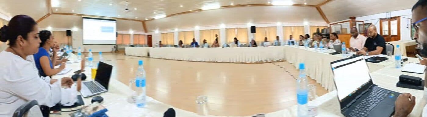 Delegates seated around a large open square of tables at the Ministry of Employment and Human Resource Planning consultation workshop, laptops and water bottles in front of them.