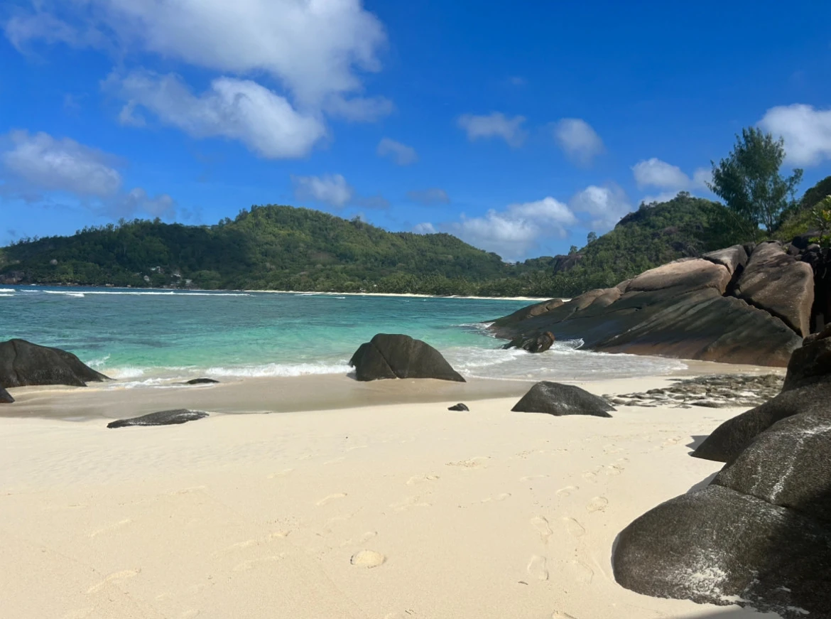 Granite boulders beside a sandy beach, turquoise sea and wooded hills